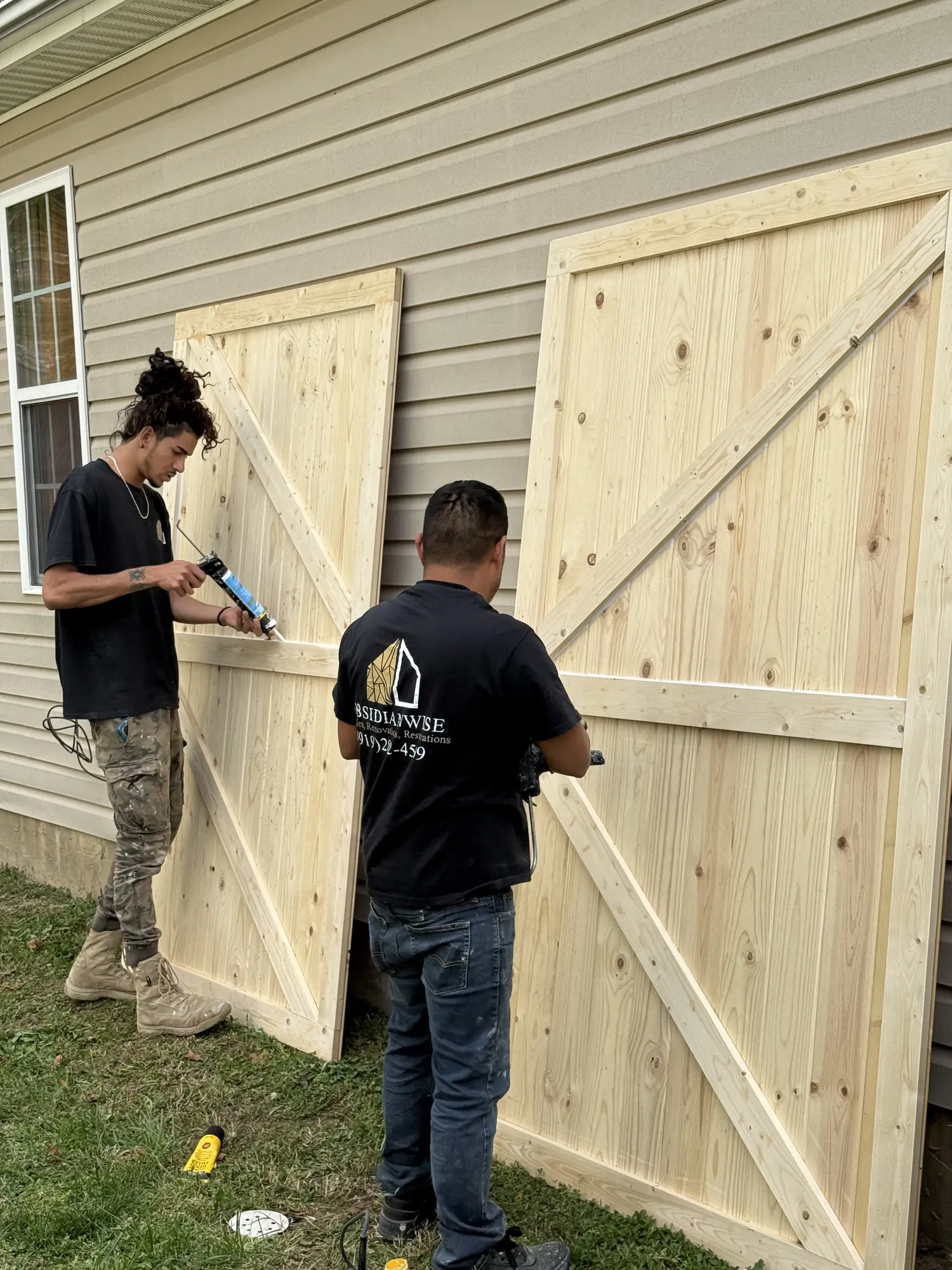 Two Obsidianwise crew members building custom barn doors outside a client's house