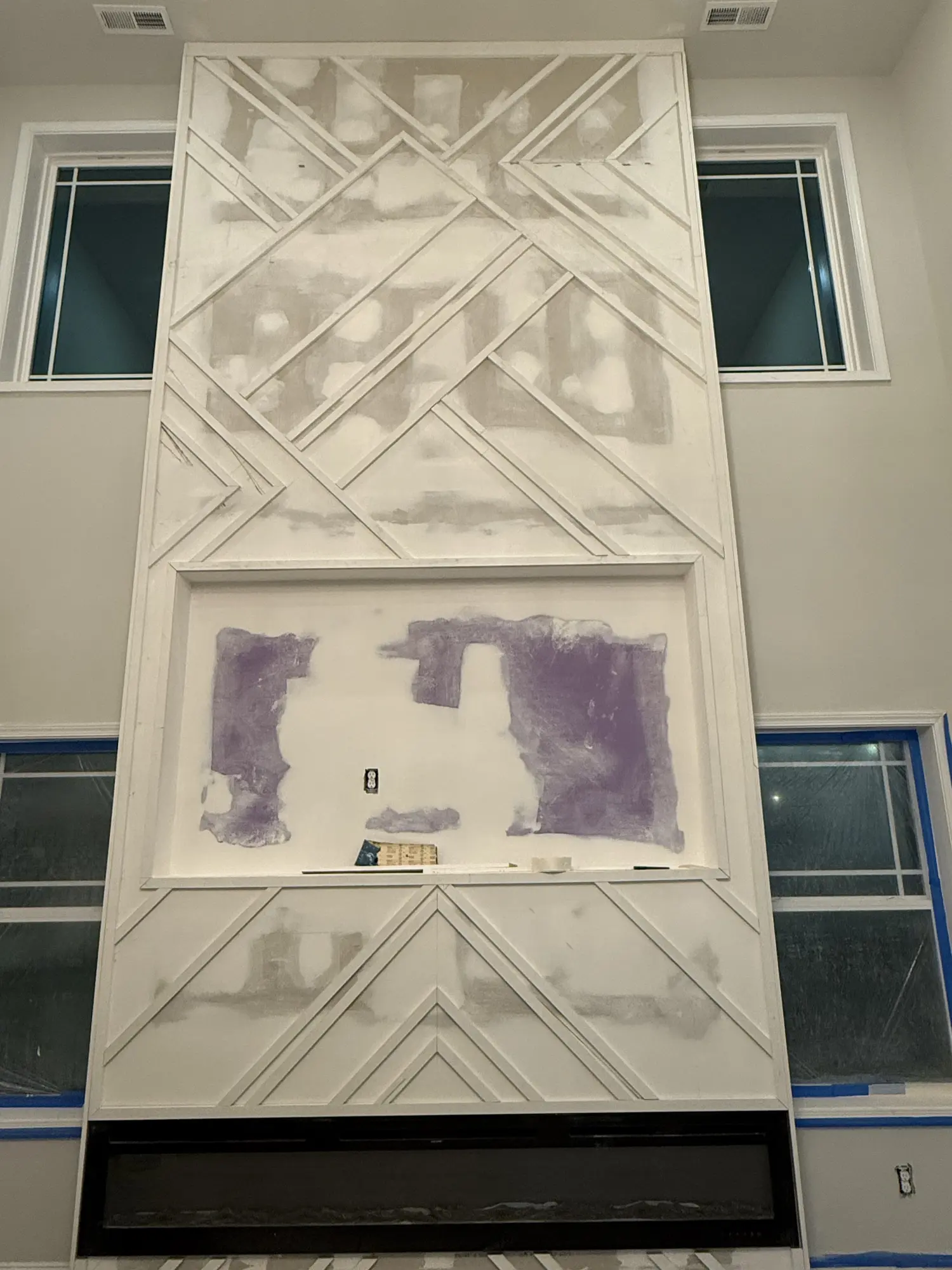 Two story fireplace wall with geometric trim pattern, taped and ready for paint