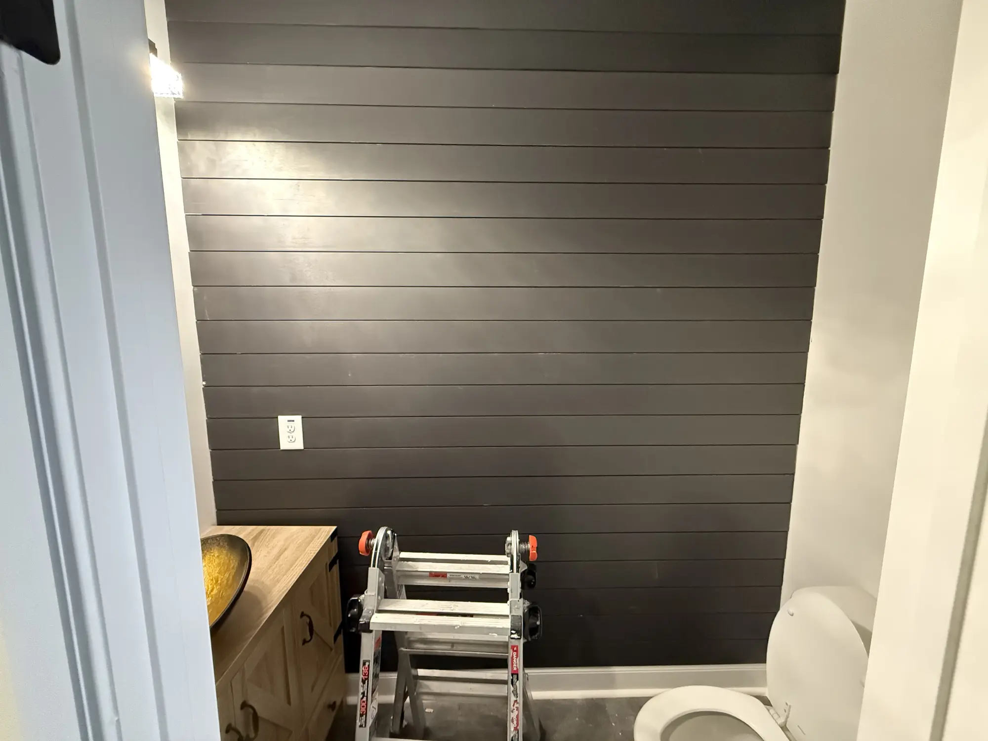 Dark shiplap accent wall being installed in a bathroom, ladder still in place
