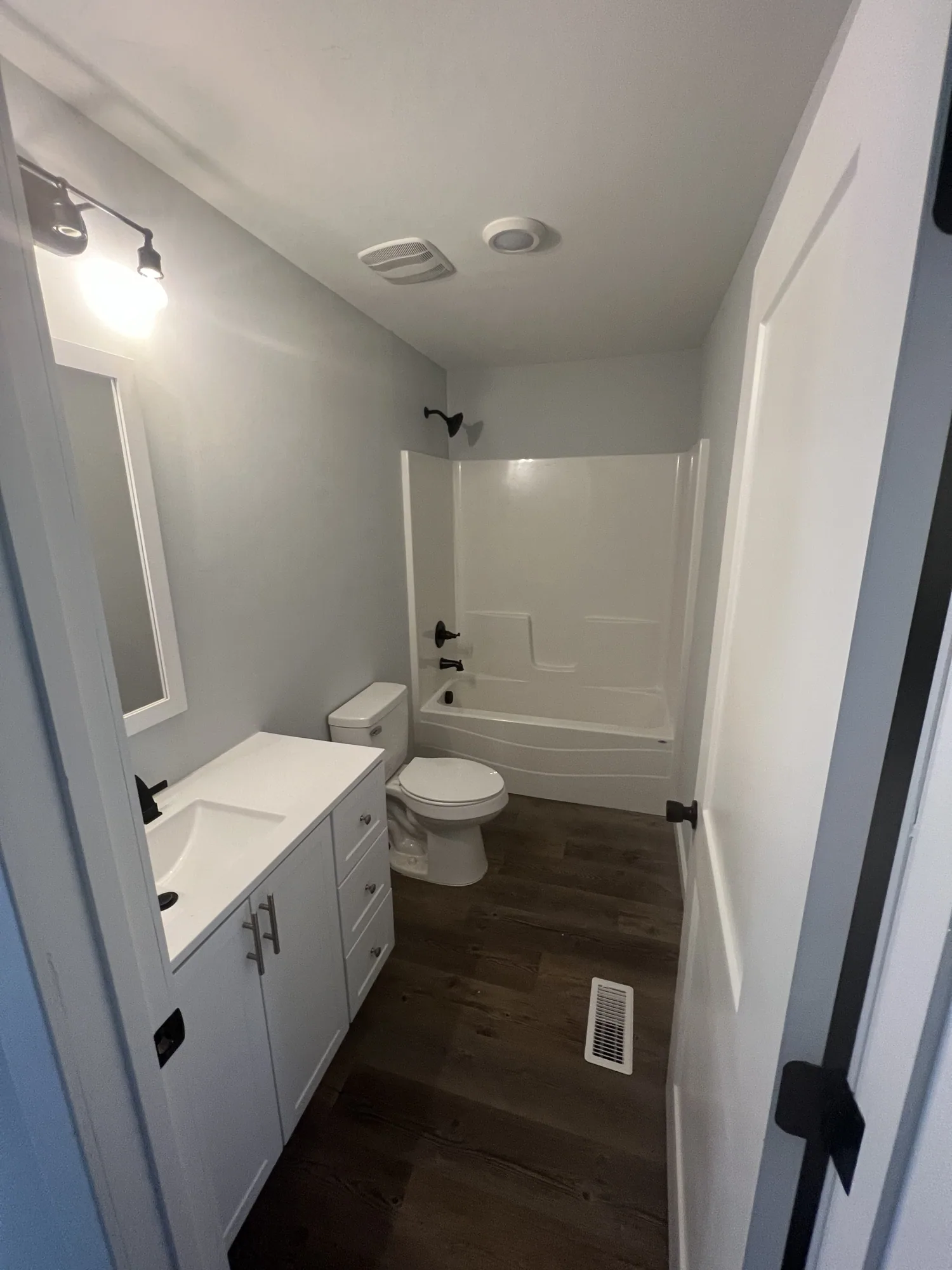 Finished bathroom with a white vanity, black fixtures, tub and shower and dark plank floor