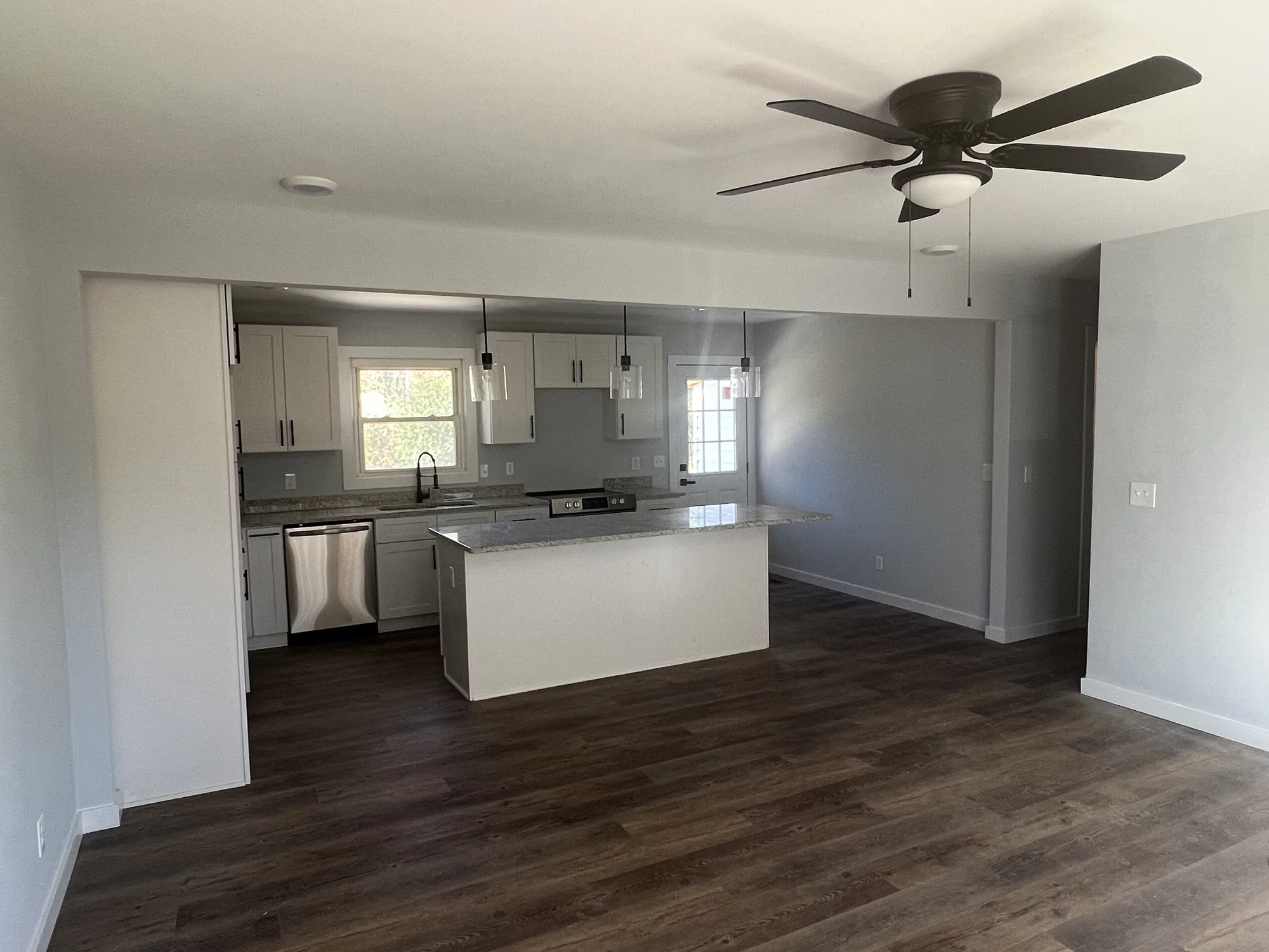 Finished open-plan living room and kitchen with white cabinets, granite counters and dark wood-look plank flooring