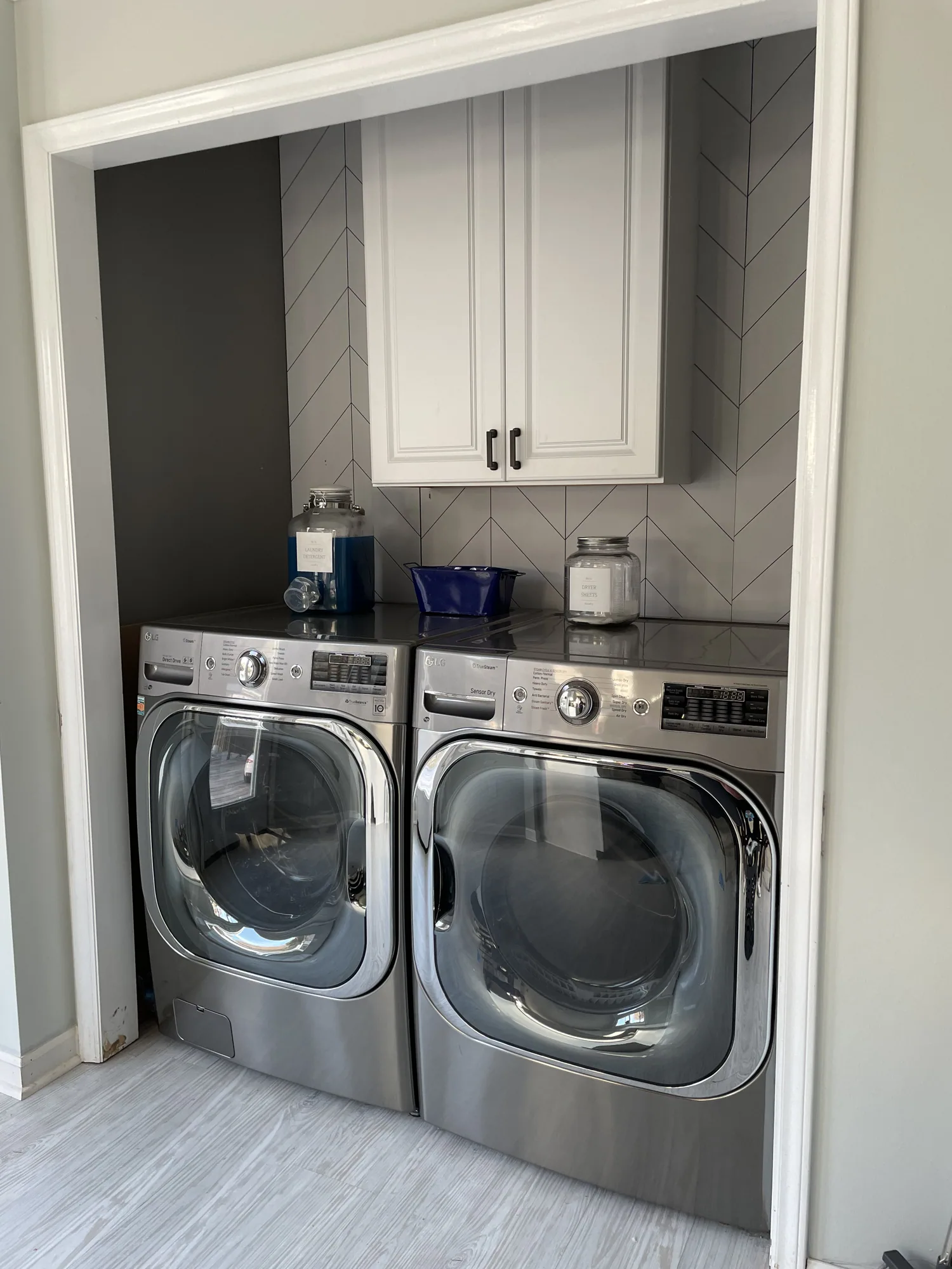 Laundry nook with a herringbone tile wall, new white wall cabinet and washer and dryer