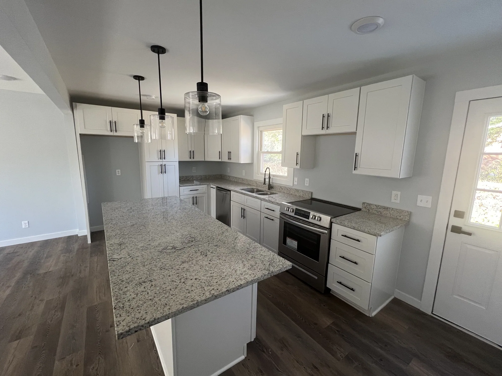 New white shaker kitchen with a granite island, pendant lights, stainless range and dark plank floor