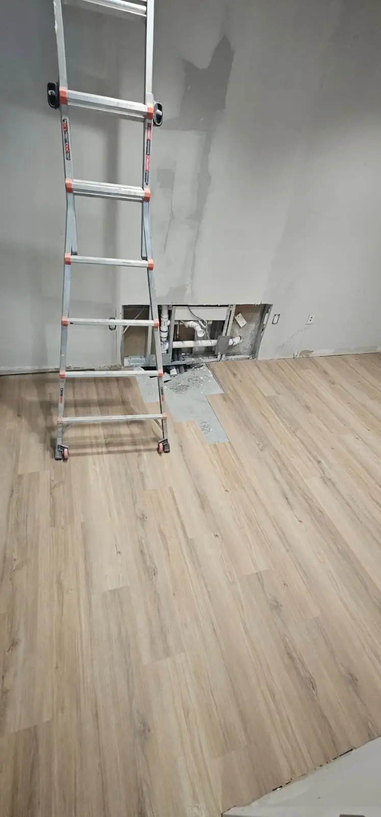 Room with fresh luxury vinyl plank flooring and a ladder against a patched wall