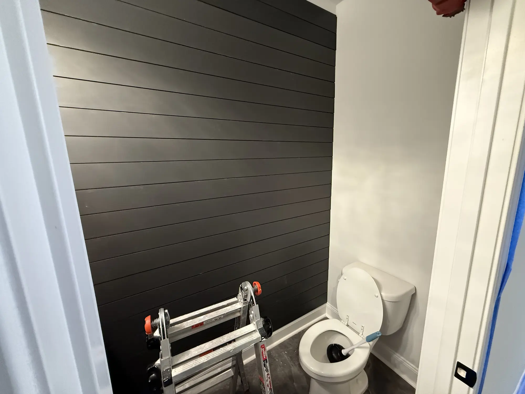 Dark shiplap accent wall installed in a bathroom, ladder still in the room