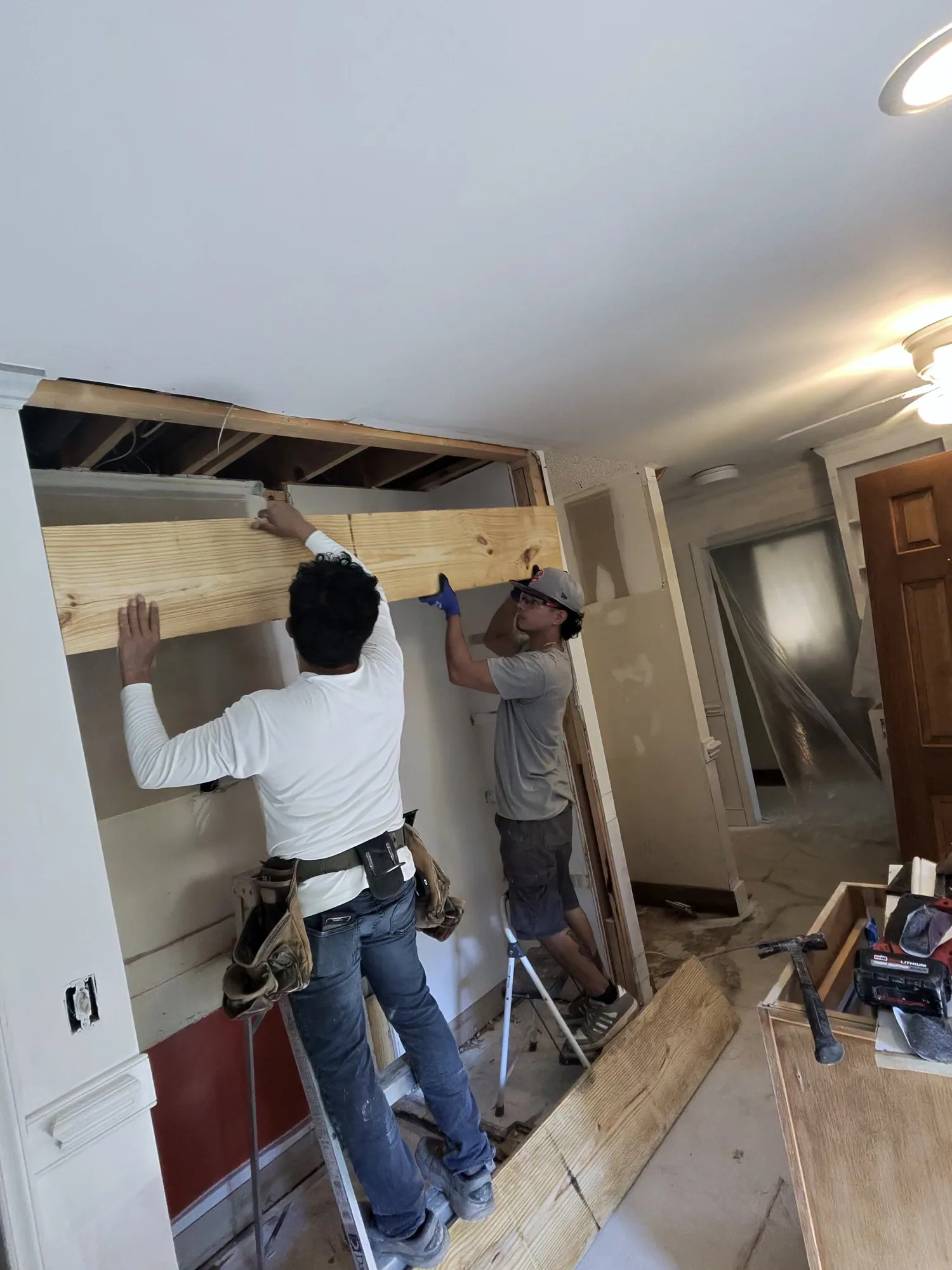 Two Obsidianwise team members on ladders fitting a new timber header beam in an opened-up wall
