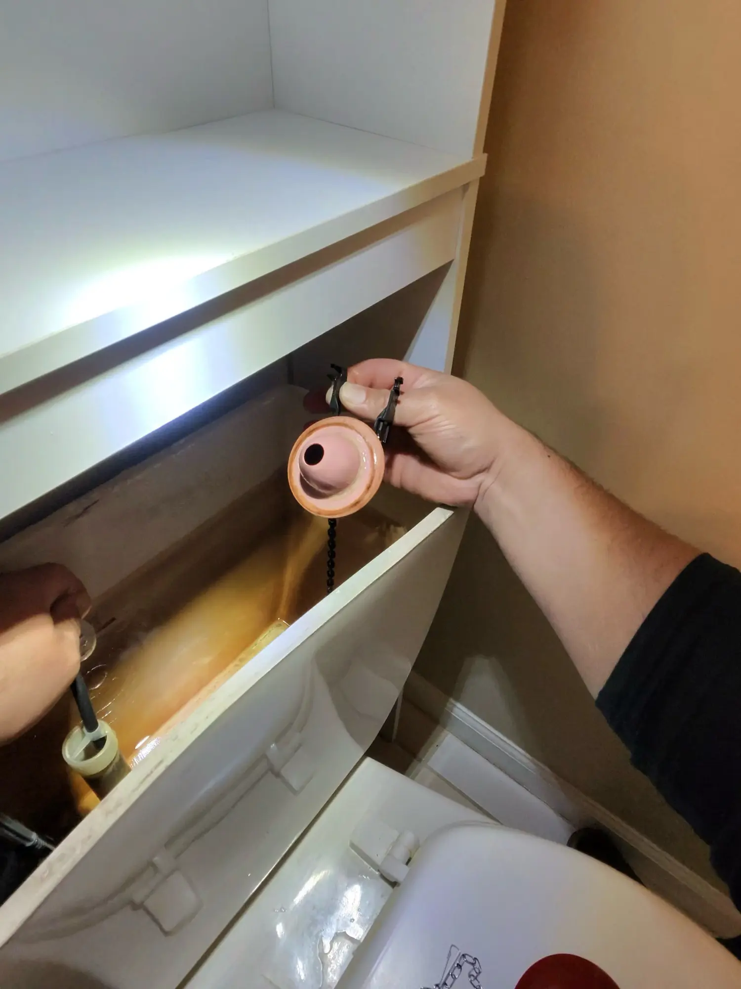 Toilet tank internals being repaired by hand