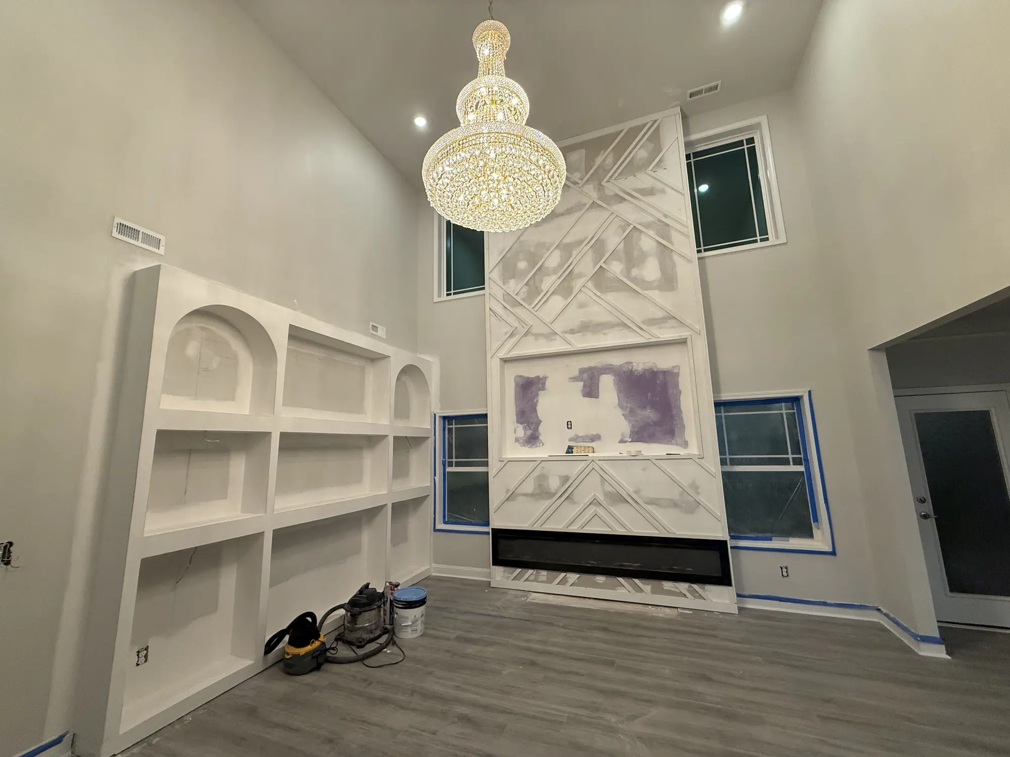 Two story living room with custom built-in shelving and a chandelier, mid build