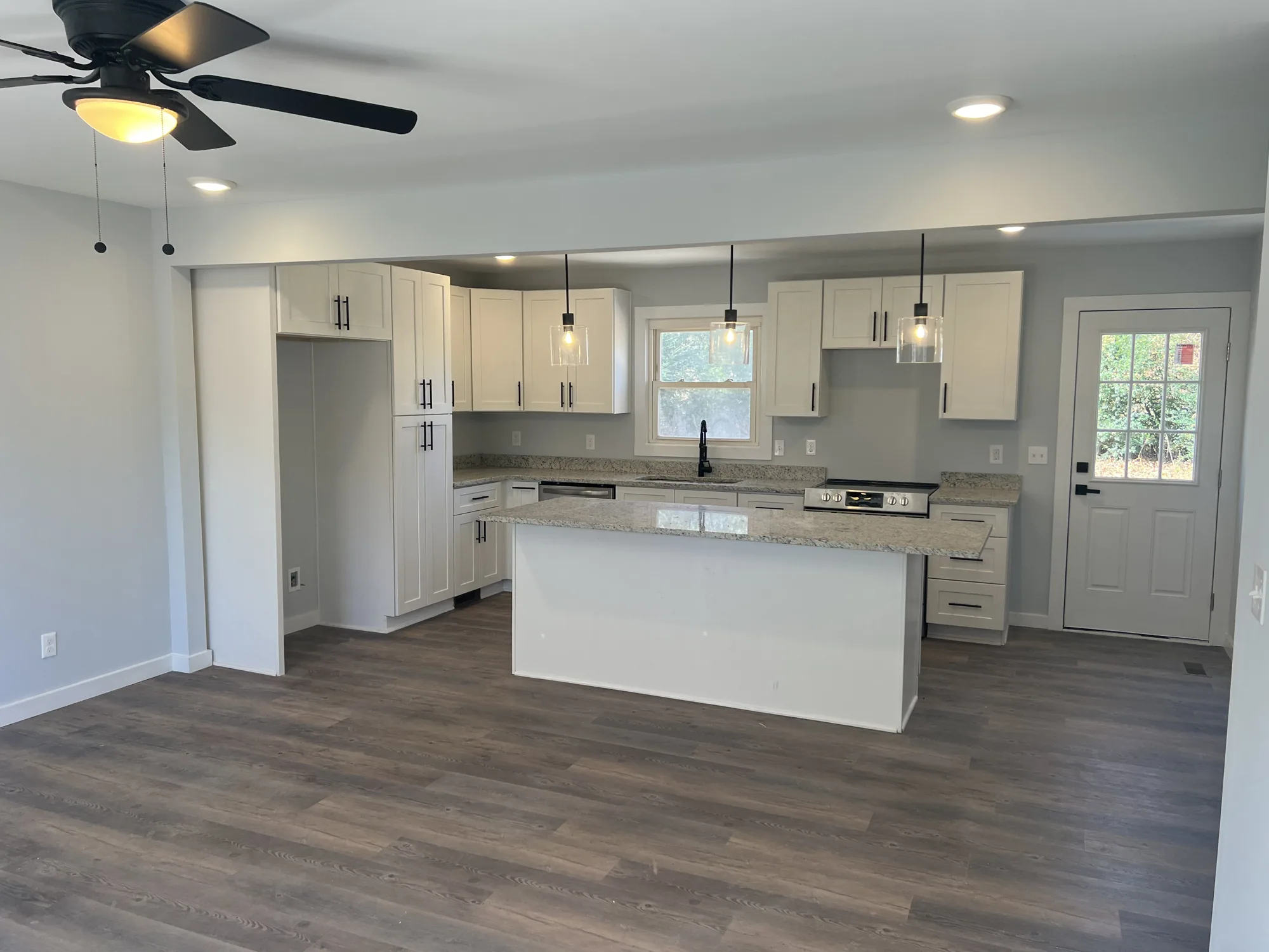 White kitchen with an island, granite counters, glass pendant lights and dark plank flooring